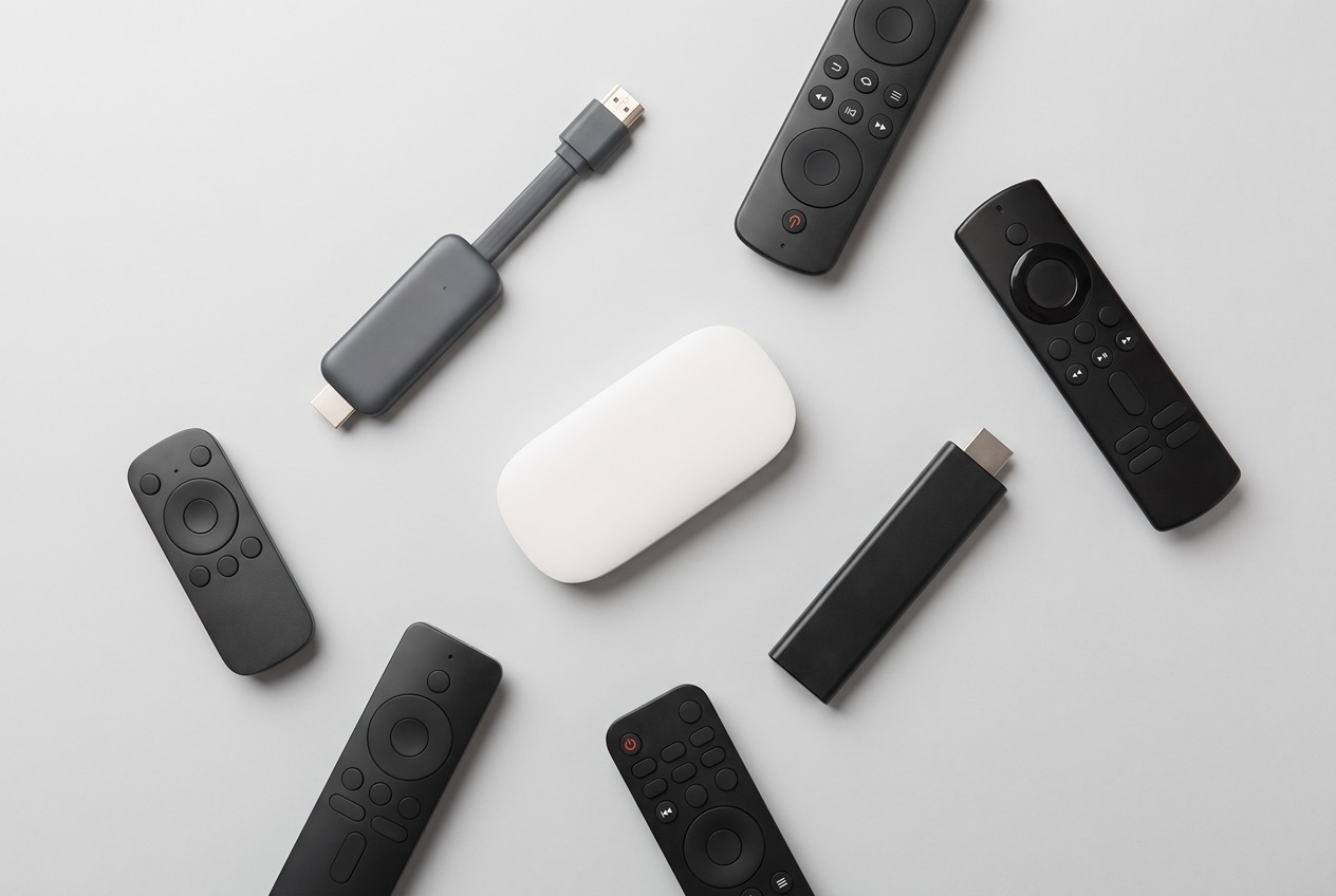 Verschiedene TV Sticks und Streaming-Geräte im Vergleich mit ihren Fernbedienungen vor einem Fernseher